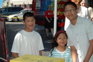 Asian brothers smiling with their younger sister near ABC Library vehicle.