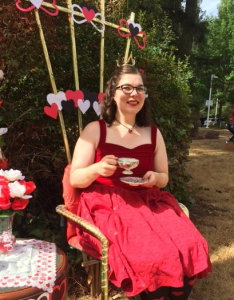 Peggy dressed as the Queen of Hearts from Alice in Wonderland, sitting in a fancy chair sipping tea